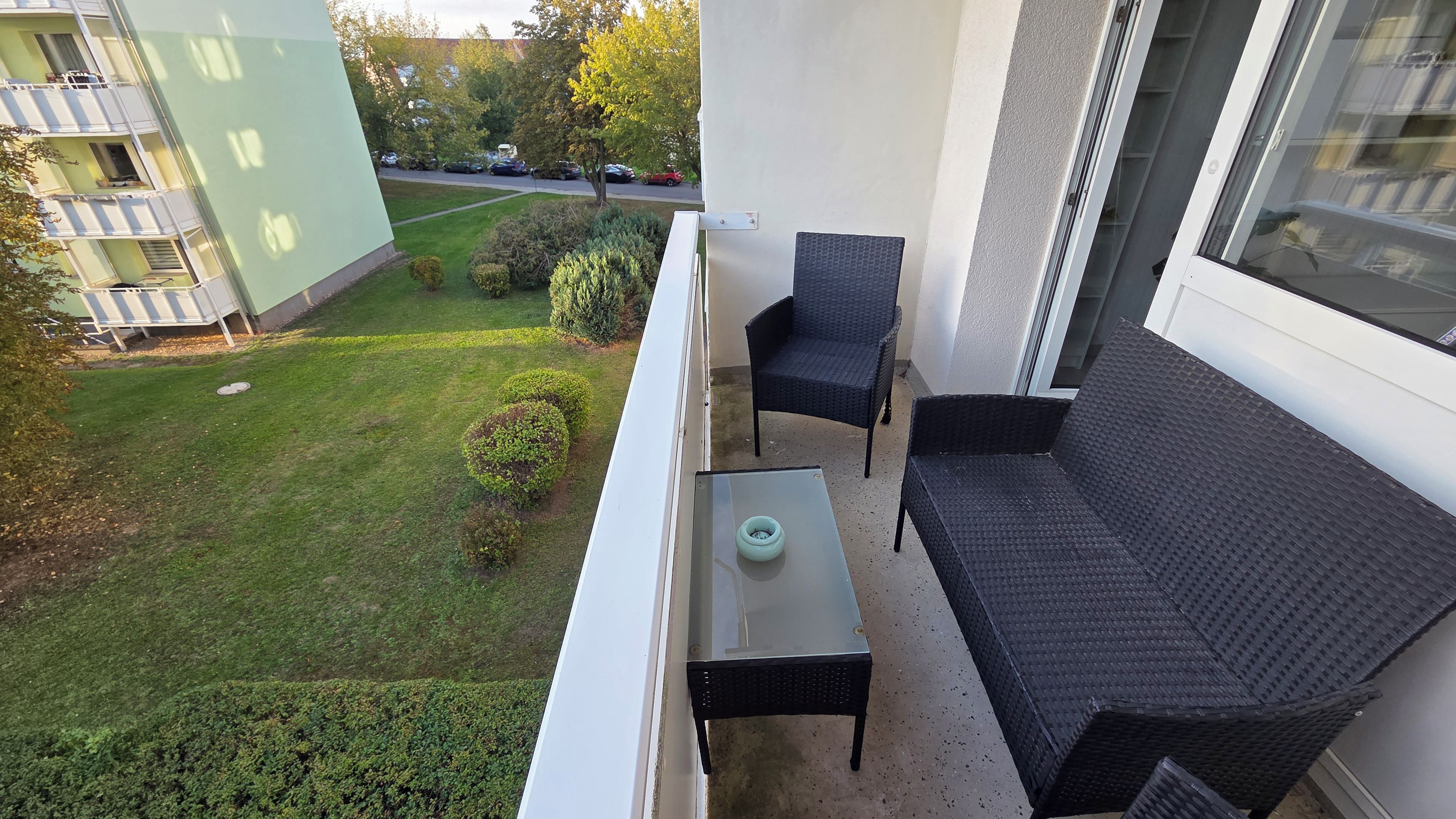 A balcony with a black wicker sofa, a small table, and a glass-top table.