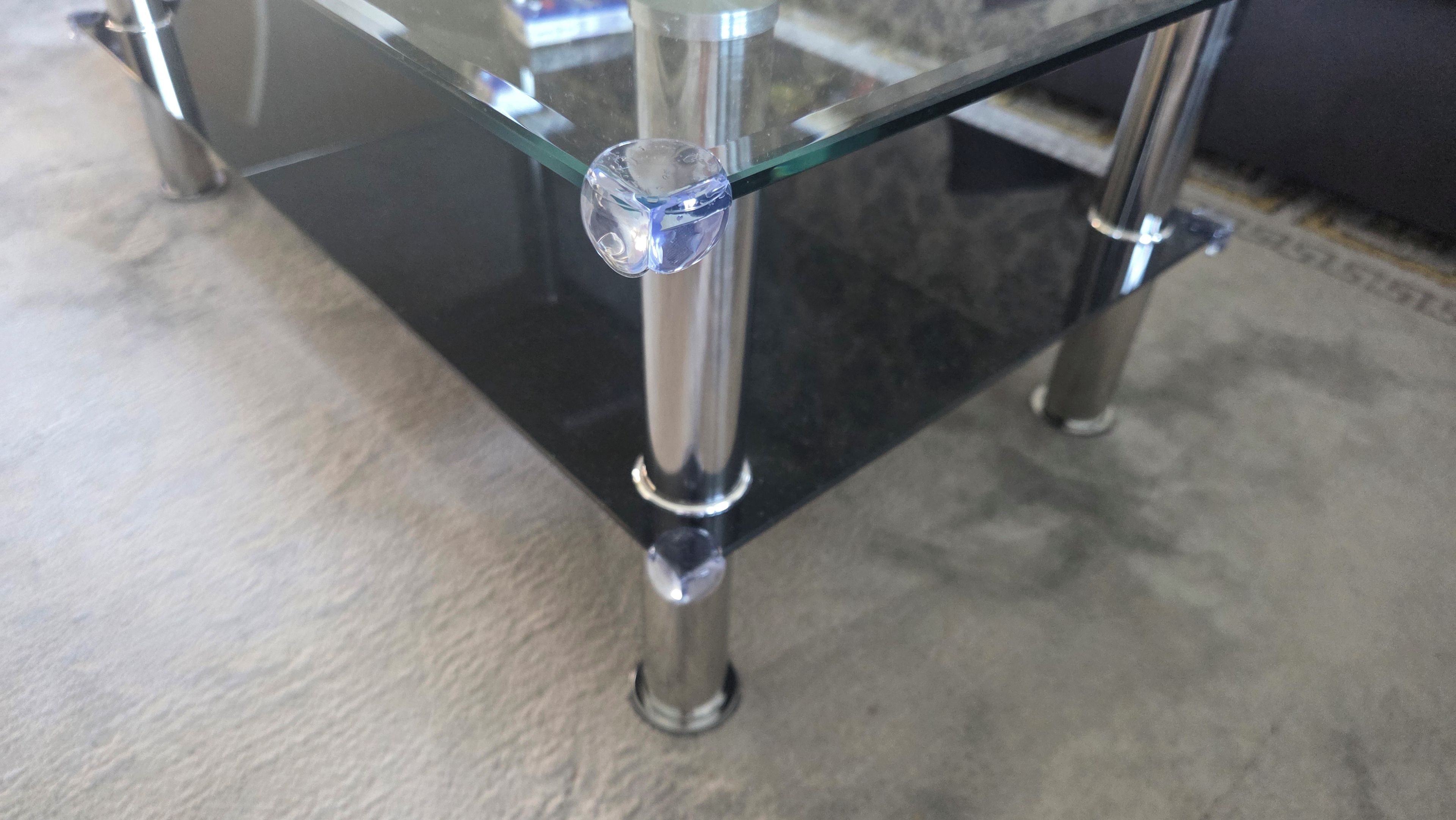 A glass-top table with metal legs, a clear glass object on the table, and a concrete floor.
