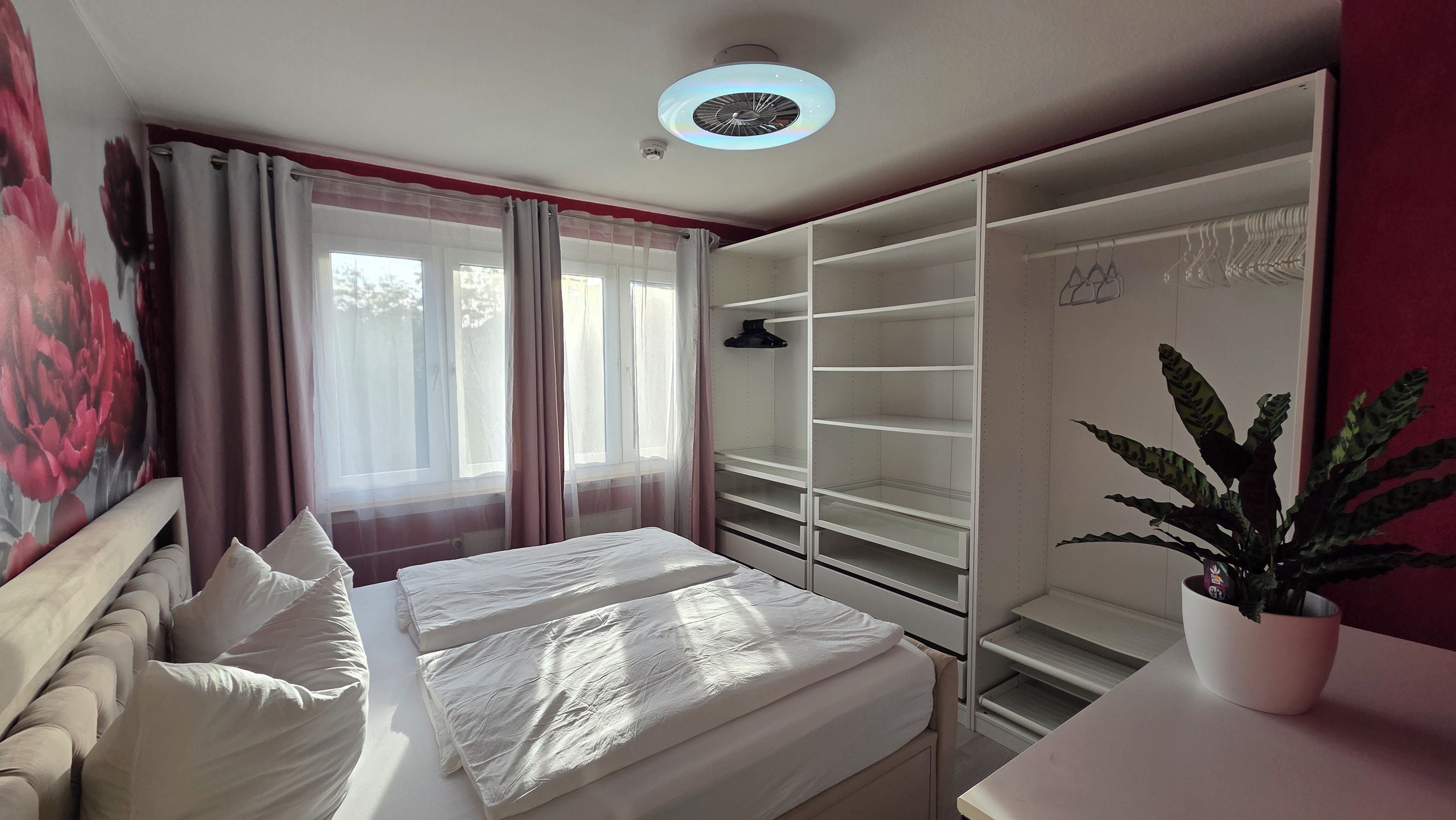 A bedroom with a bed, a wardrobe, a desk, and a potted plant.