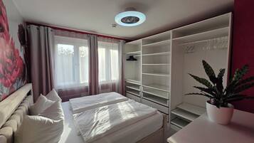 A bedroom with a bed, a wardrobe, a desk, and a potted plant.
