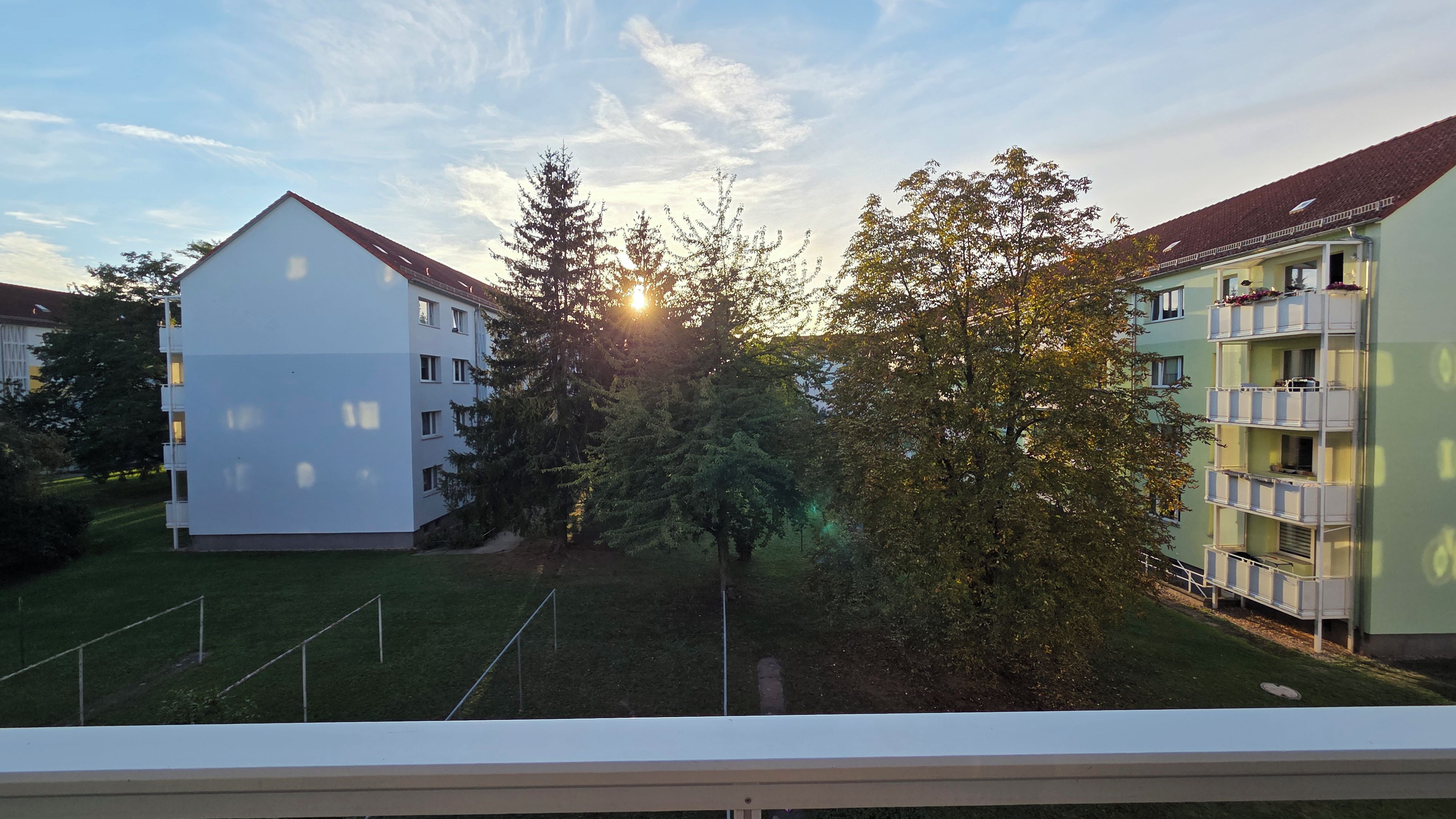 Ein Wohngebäude mit mehreren Balkonen, einem Rasen und Bäumen.