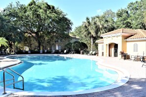 A swimming pool with a tiled deck, surrounded by lounge chairs and palm trees. - Disney Family Townhouse Heated Pool Gated Community (Kissimmee)