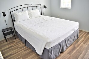 A neatly made bed with a white quilt and grey skirt, a small bedside table with a lamp, and a wooden floor. - Disney Family Townhouse Heated Pool Gated Community (Kissimmee)