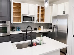 Una cocina moderna con electrodomésticos de acero inoxidable, encimera blanca y una vinera empotrada.