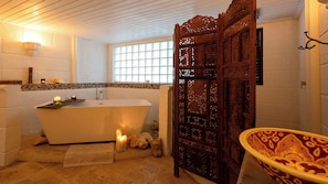 A bathroom with a freestanding bathtub, a wooden door with intricate carvings, and a window providing natural light. - Dragonfly Villa - By Zenbreak (Holetown)