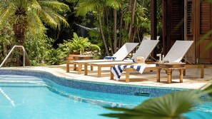 Un espace piscine aménagé avec des chaises longues, une table en bois et un bord carrelé.