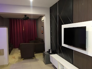 A modern living room with a flat-screen TV mounted on the wall, a sofa, a coffee table, and a small cabinet.
