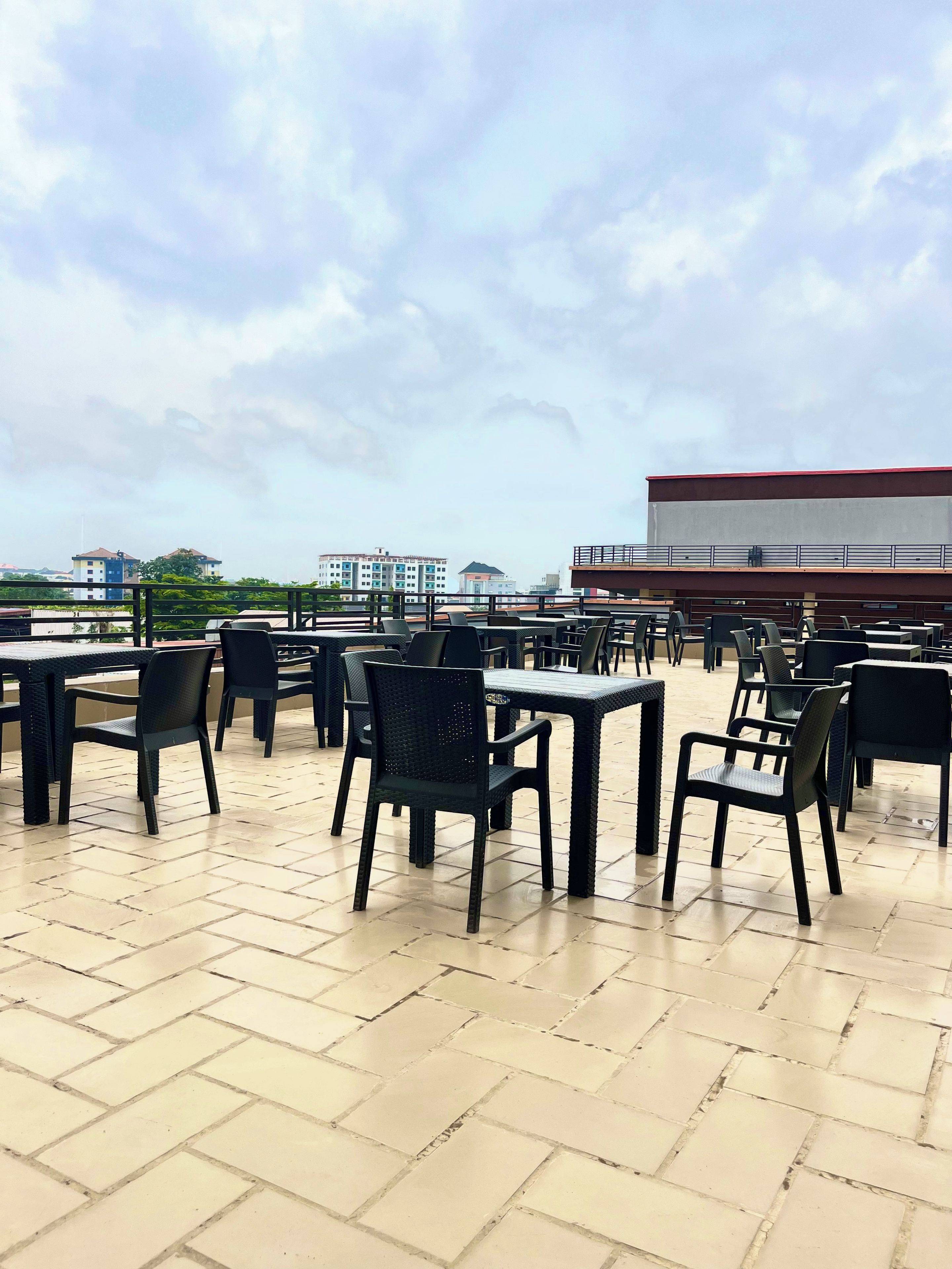 Un área de estar al aire libre con mesas y sillas, piso de baldosas y vistas a edificios distantes.