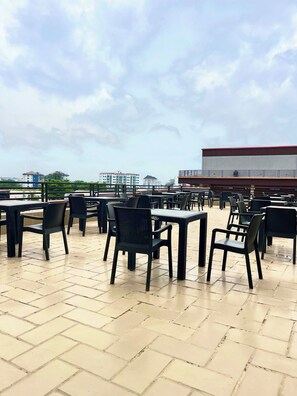An outdoor seating area with tables and chairs, a tiled floor, and a view of buildings in the distance. - Soul Lounge Resort (Abuja)