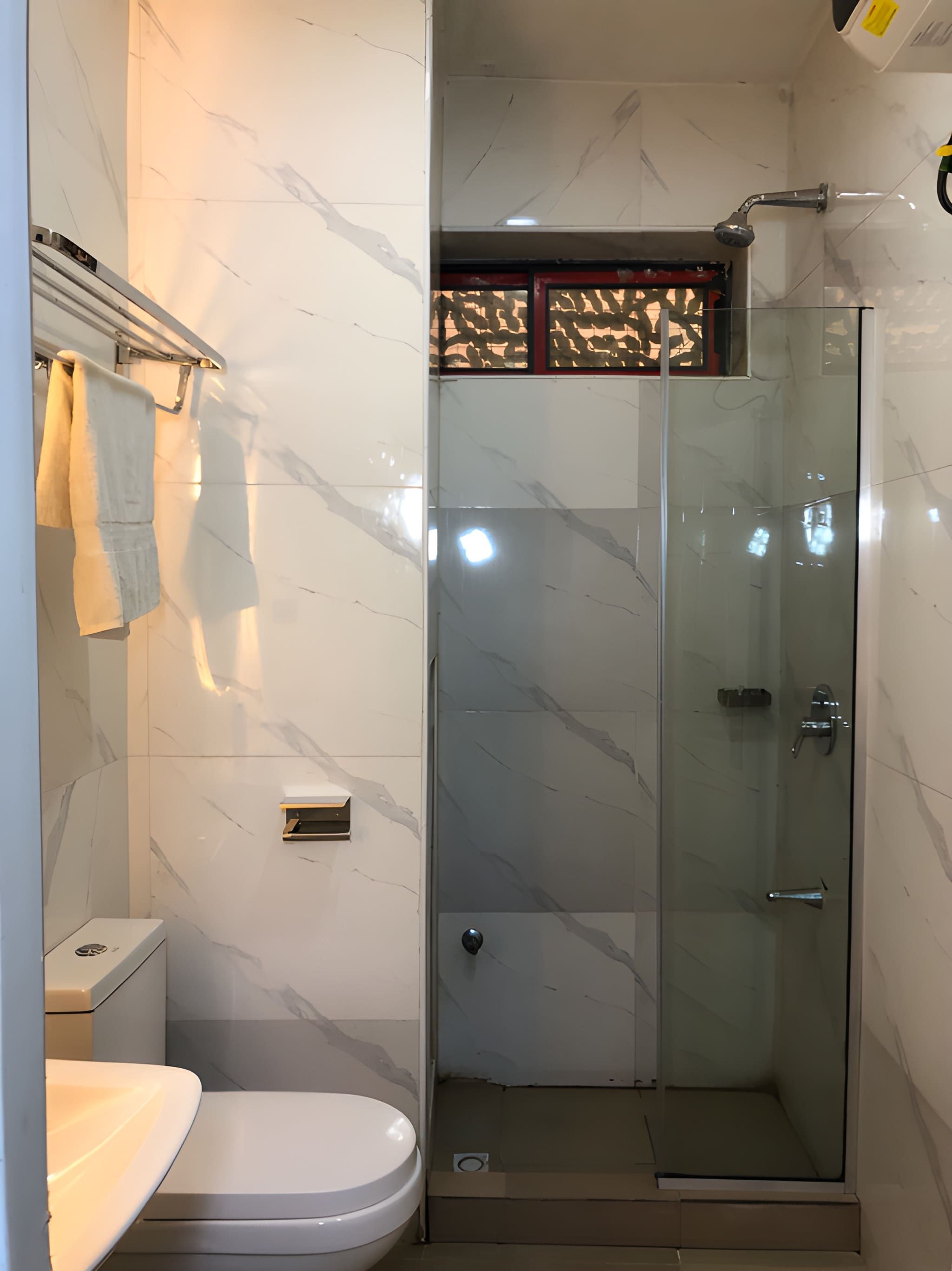 Un baño con ducha envuelta en vidrio, inodoro y toallero.