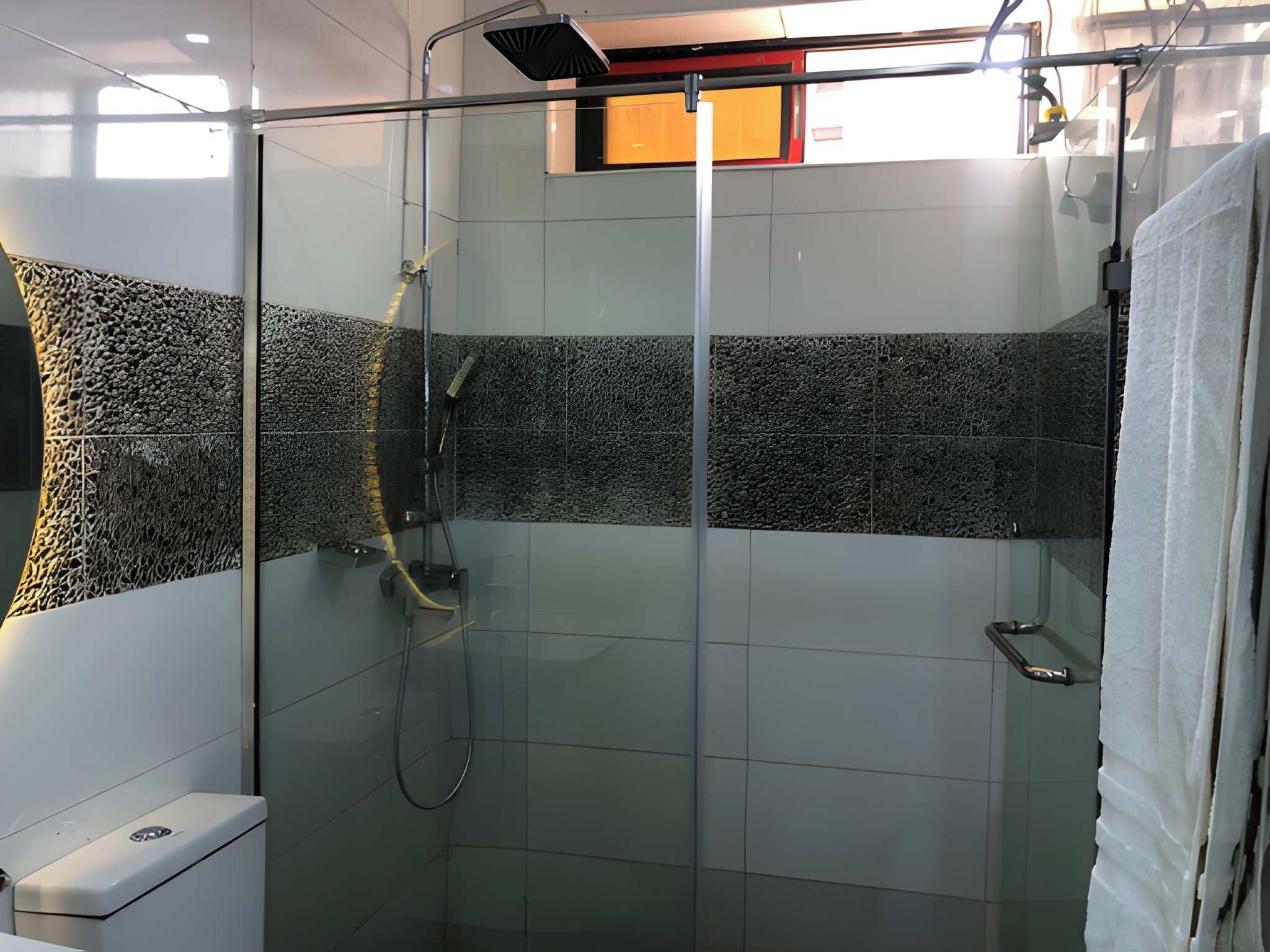 Un área de ducha moderna con mampara de vidrio, un cabezal de ducha manual y un panel de control en la pared.