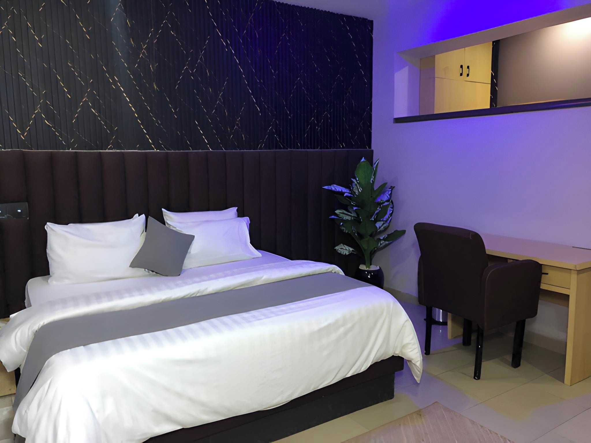A modern hotel room with a bed, a desk, and a potted plant.