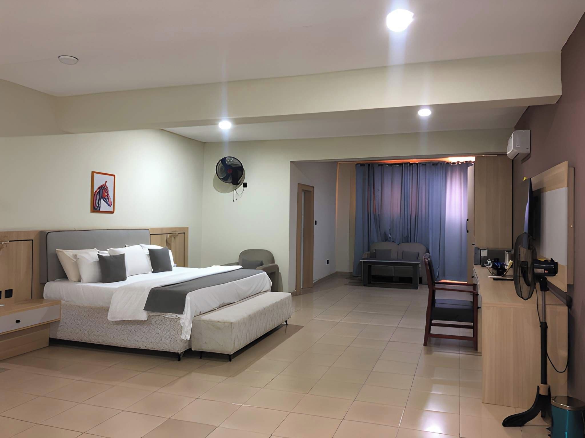 Una habitación de hotel con cama, escritorio, silla, televisor y ventilador.