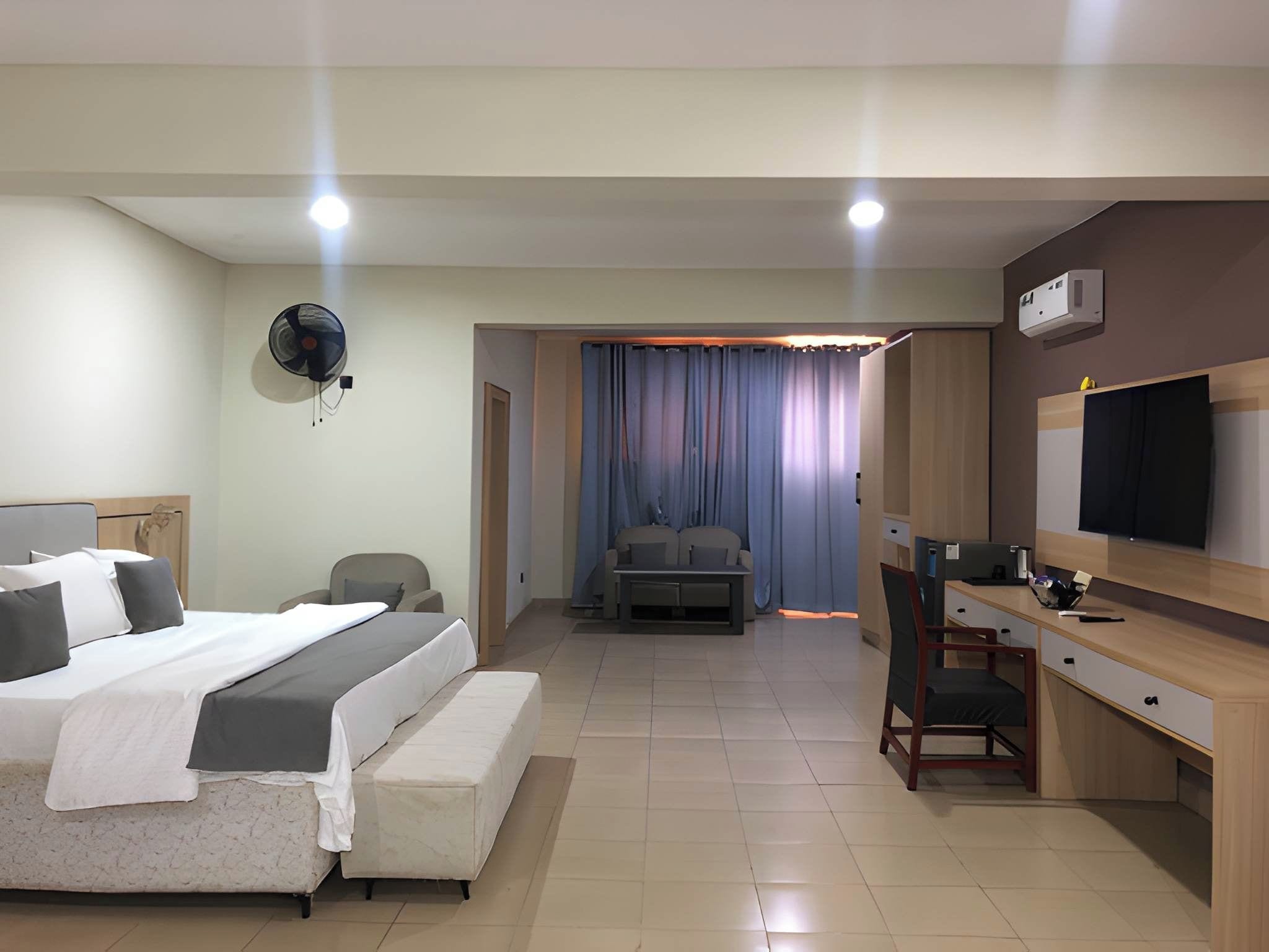 Habitación de hotel con cama, escritorio, silla, televisor y ventilador de techo.