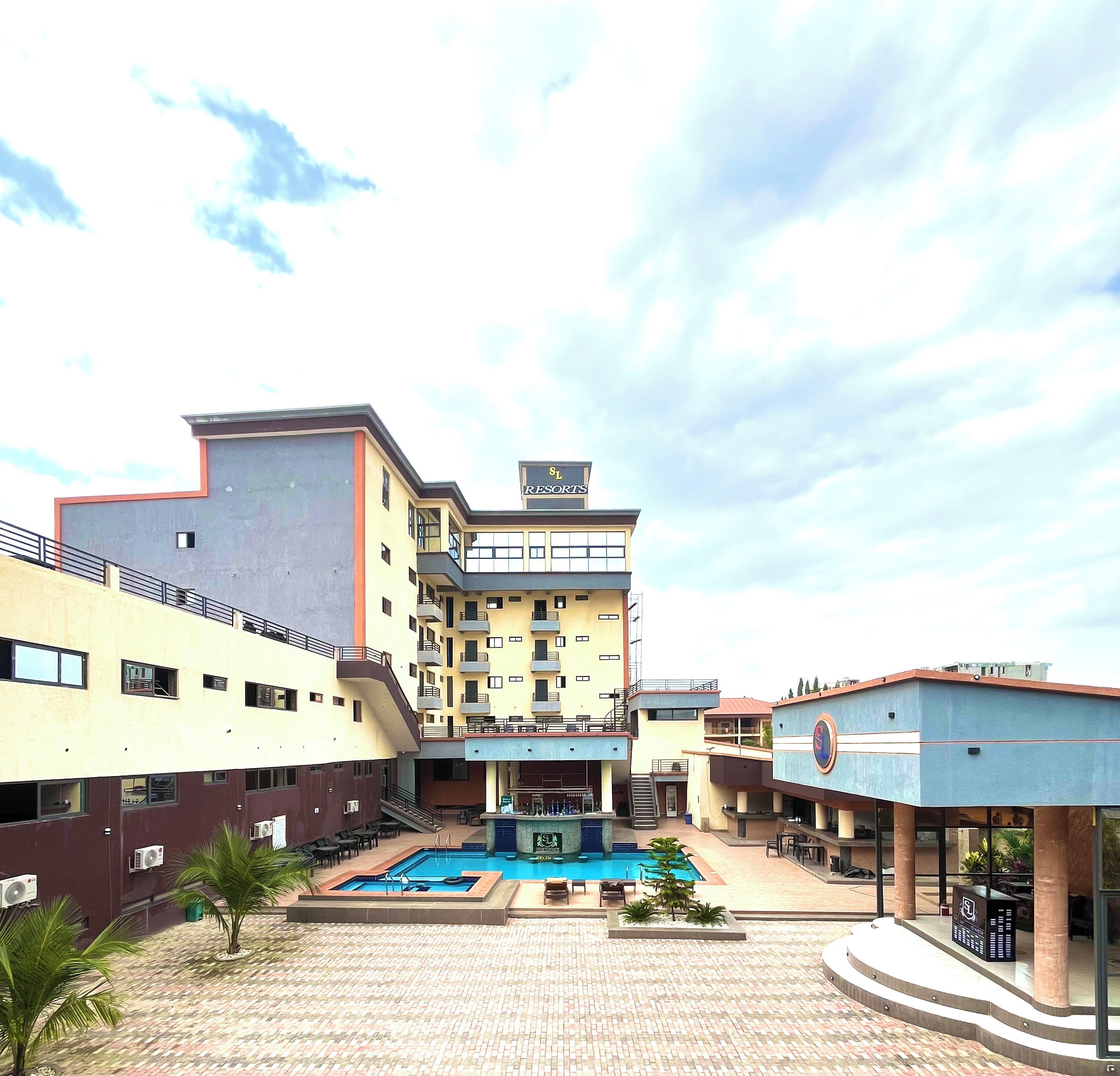 Un edificio de varios pisos con piscina, mobiliario exterior y cielo despejado.