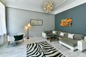A modern living room with a glass dining table, a sofa set, a zebra-patterned rug, a floor lamp, and a wall with abstract art. -  King of Church Budapest- Church-View Balcony Apartment  in Central Budapest (Budapest)