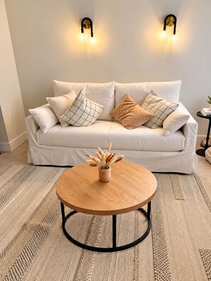 A living room with a white sofa, two wall-mounted lights, a round wooden coffee table, and a textured rug. - 24th Floor 1-bedroom Full Kitchen Washer/Dryer Sunny Isles Direct Beach Access (Sunny Isles Beach)