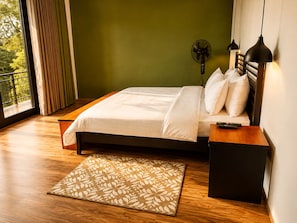 Un dormitorio con cama, mesitas de noche, un control remoto, un ventilador y una ventana con cortinas.