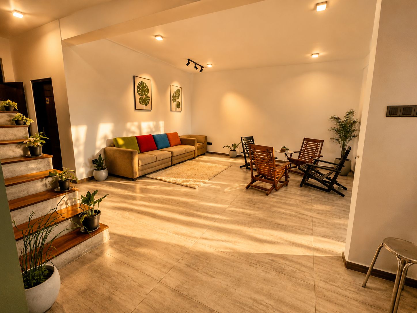 Un amplio salón con sofá, sillones y una escalera decorada con plantas en macetas.