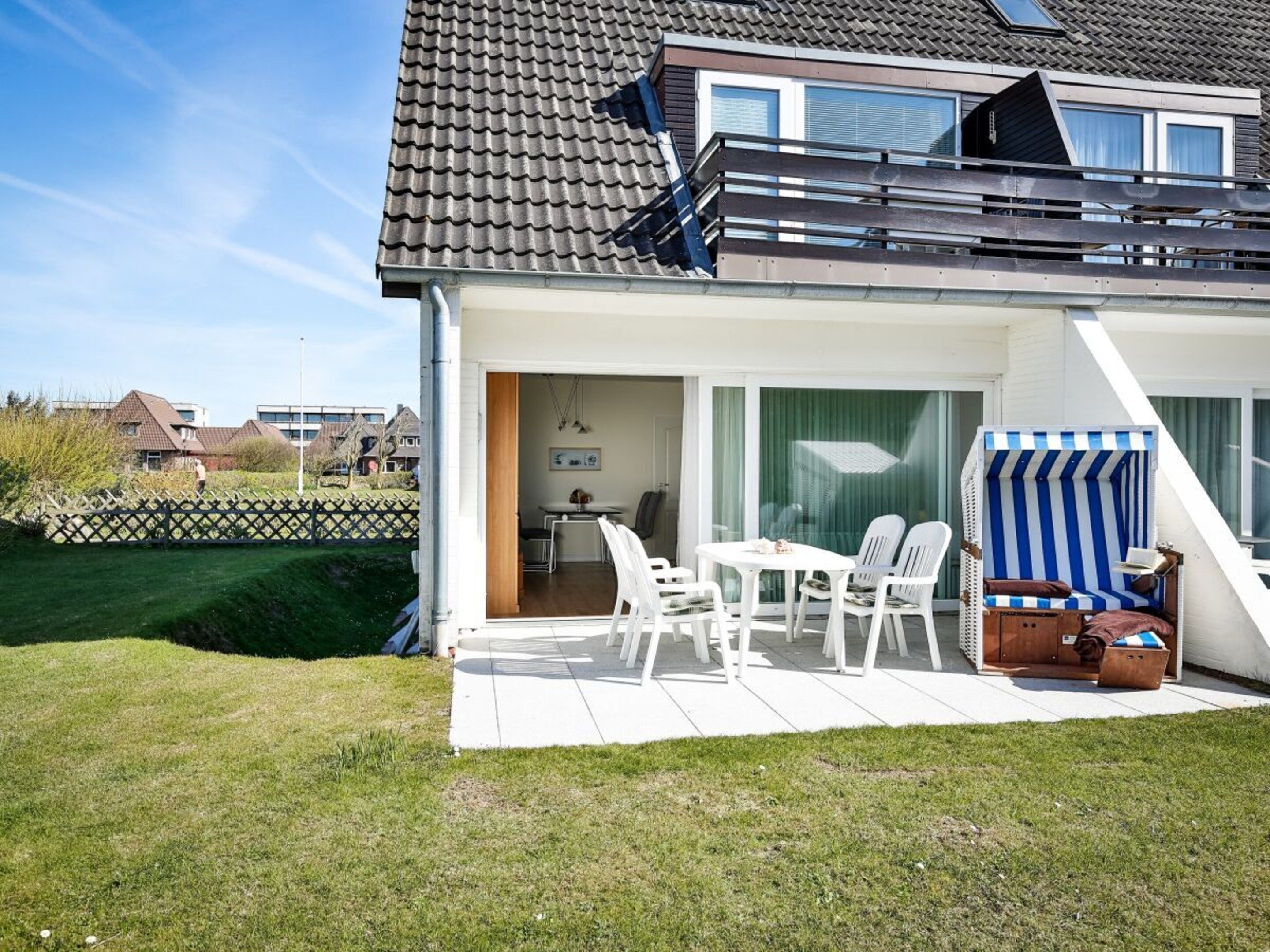 Ein modernes Haus mit einer Terrassenfläche, einem Essplatz und einem gestreiften Liegestuhl.