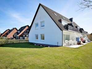 Ein modernes Haus mit geneigtem Dach, einer überdachten Terrasse mit Gartenmöbeln und einem gepflegten Rasen.
