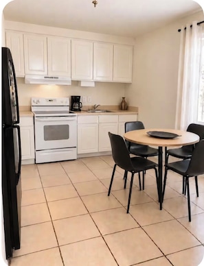 A compact kitchen with white cabinets, a stove, a coffee maker, and a dining area with a round table and four chairs. - 2-bedroom apartment in excellent Phoenix with refreshing AC (Phoenix)