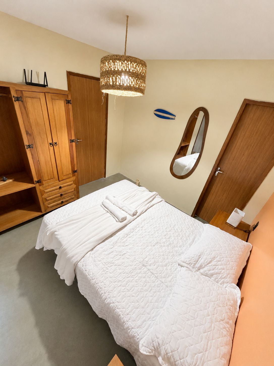 A bedroom with a bed, a wardrobe, a mirror, and a hanging light fixture.
