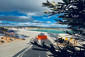 Zona de piscina amb gandules i un espai d'seure petit i taronja, amb vista a una platja i al mar.