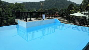 Una piscina con barandilla negra, un cartel que indica que la piscina está cerrada y una vista de una colina con árboles al fondo.