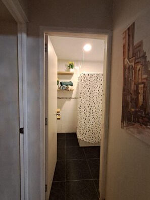 A hallway leading to a bathroom with a shower curtain, a towel rack with folded towels, and a painting on the wall. - New Listing (Miraflores)