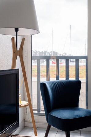 Une pièce avec une télévision, une lampe et une chaise près d’une fenêtre donnant sur un paysage de bateaux.