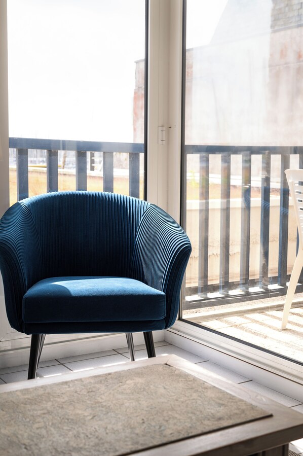 Un fauteuil bleu recouvert de tissu, doté d’un motif côtelé original, placé sur un balcon d’où l’on peut admirer un immeuble et une balustrade.