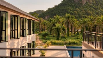 A modern building with large windows, a pool, and a view of a lush green landscape with palm trees.
