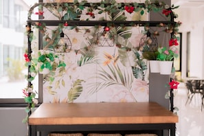A wooden bench with a floral wallpaper backdrop, a hanging light fixture, and a potted plant.
