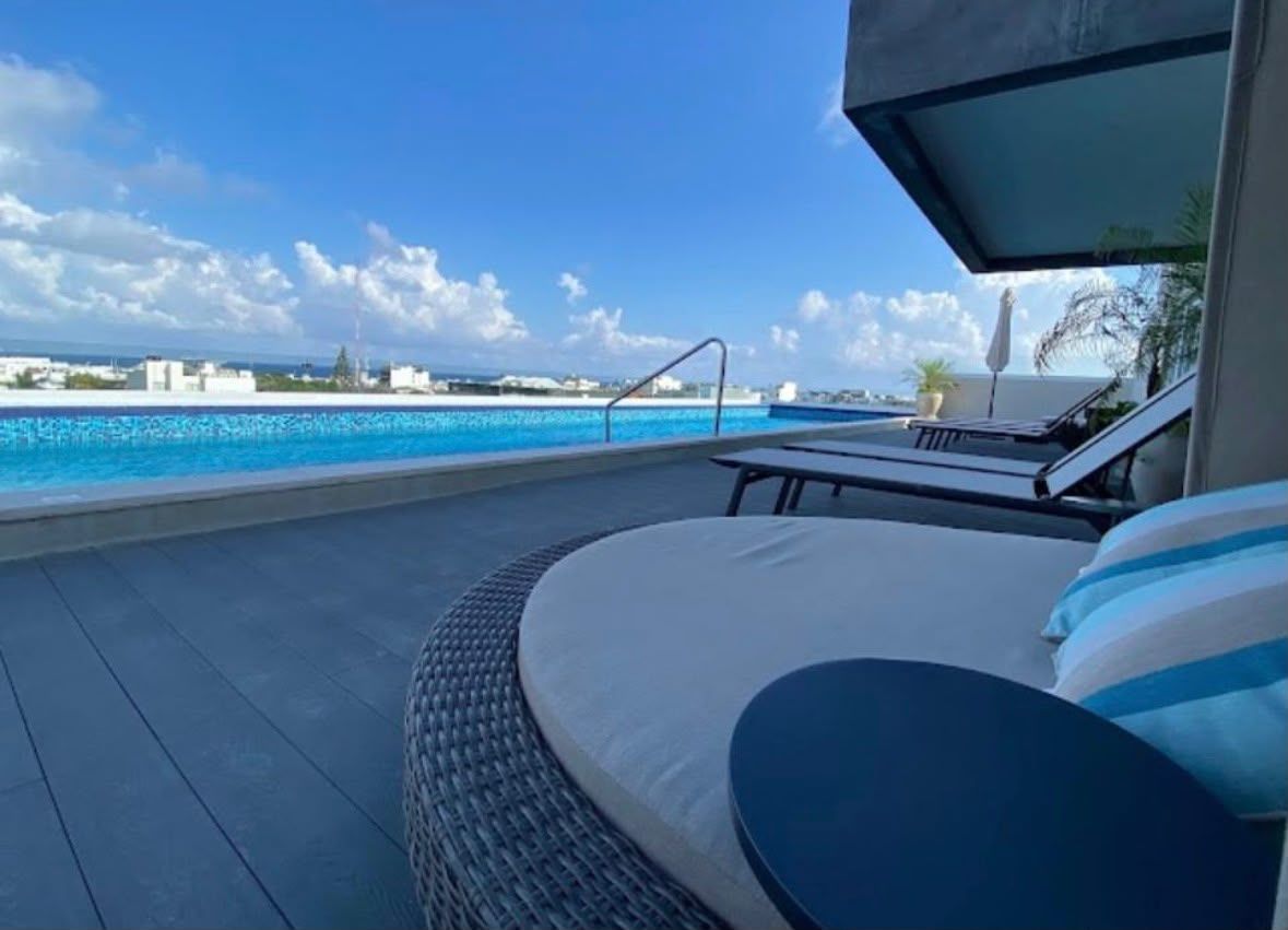 Un espace aménagé au bord de la piscine, avec un fauteuil de relaxation et une chaise longue, offrant une vue sur une mer d’un bleu limpide et sur une côte lointaine.