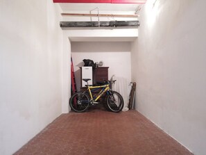 Passadís estret amb una bicicleta aparcada al mur, un armari de fusta i una escala vermella.