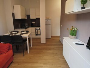 Espai habitable compacte amb petita cuina, zona de menjador i un petit seient amb un sofà vermell.