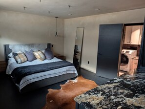 A modern bedroom with a bed, a mirror, a wardrobe, and a washing machine in the background. - Tiki Oasis at Indian Circle (Kennesaw)