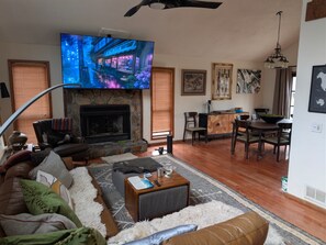 A living room with a fireplace, a television mounted on the wall, and a dining area with chairs and a table. - Tiki Oasis at Indian Circle (Kennesaw)