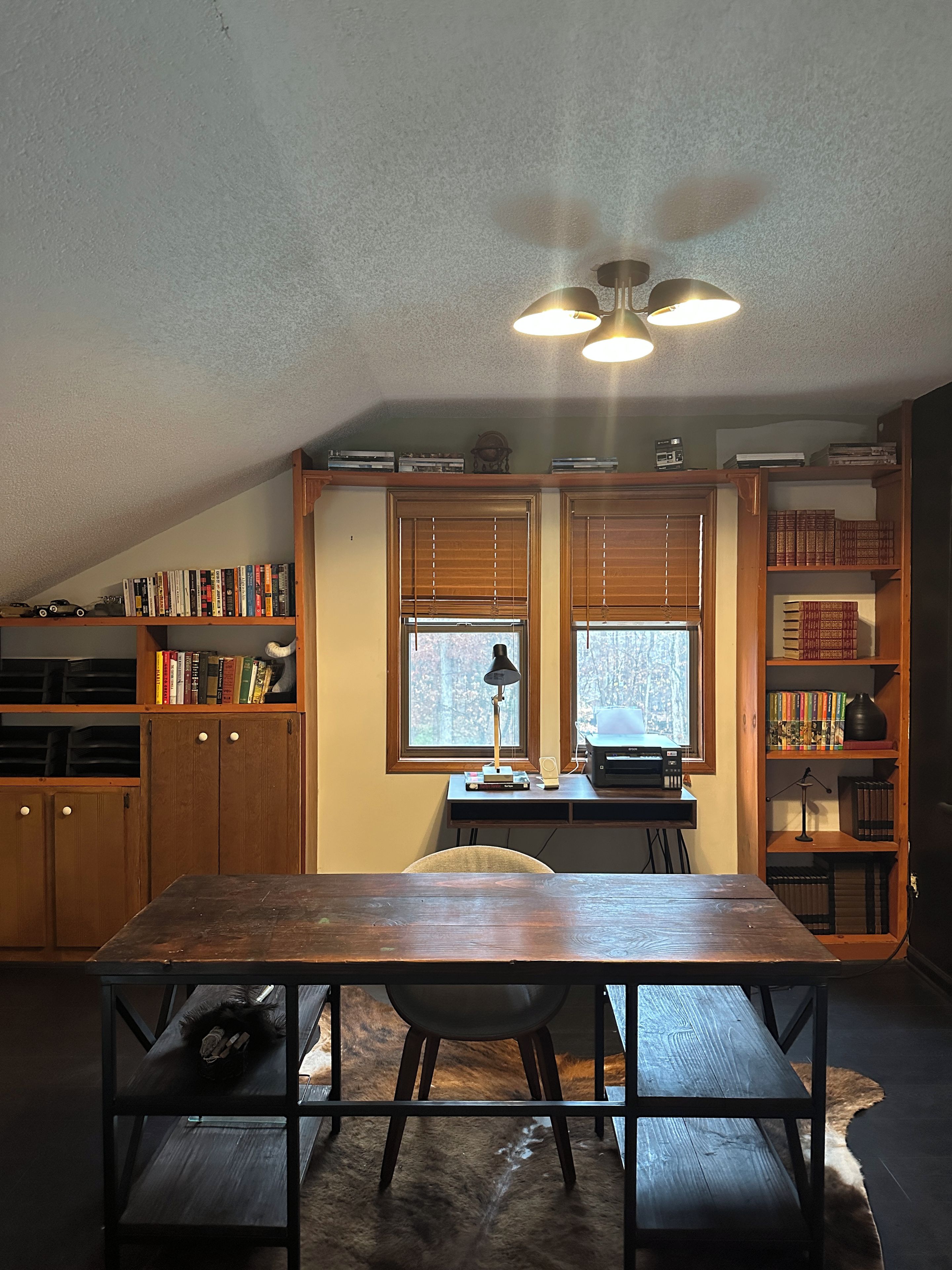 Um quarto aconchegante com uma mesa de madeira, estantes de livros, uma escrivaninha e uma janela com persianas.