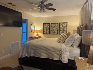 A bedroom with a bed, a ceiling fan, a TV, a bedside table, and artwork on the wall. - Gorgeous 3-bedroom canal waterfront house (New Port Richey)