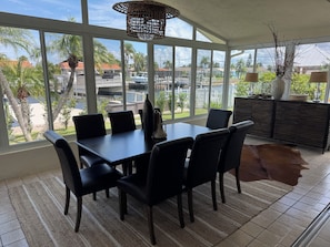 A dining area with a table and chairs, large windows, a woven light fixture, and a view of a residential area. - Gorgeous 3-bedroom canal waterfront house (New Port Richey)