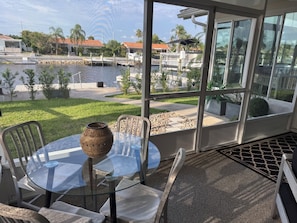 A glass table with chairs and a decorative vase, overlooking a marina with boats and a grassy area. - Gorgeous 3-bedroom canal waterfront house (New Port Richey)
