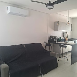 A modern kitchen with a bar area, a ceiling fan, and a black sofa. - New Listing (Itanhaém)