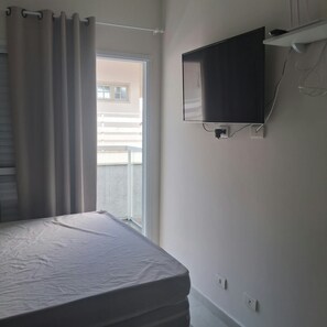 A bedroom with a bed, a window with curtains, a wall-mounted TV, and a balcony view. - New Listing (Itanhaém)