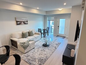 A modern living room with a sofa, a glass coffee table, and a dining area with chairs. - Scenic Kitchener Retreat | Escarpment View Balcony (Kitchener)