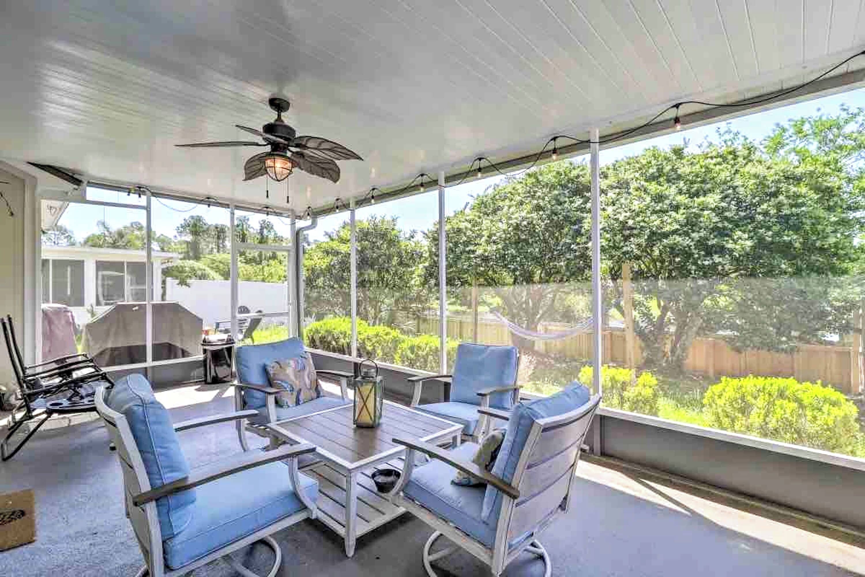 Une terrasse couverte avec une table et des chaises, de grandes fenêtres et un ventilateur de plafond.