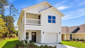 A two-story residential building with a front garage, a balcony on the upper floor, and a well-maintained lawn. - Brand-New home 5 Min to downtown, near beaches, community pool (Port St. Joe)