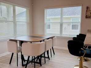 A dining area with a wooden table and chairs, large windows with blinds, and a view of the outside. - Brand-New home 5 Min to downtown, near beaches, community pool (Port St. Joe)