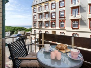 Ein Balkon mit einem Glastisch, einem Stuhl und Blick auf ein Gebäude mit mehreren Fenstern und Balkonen.